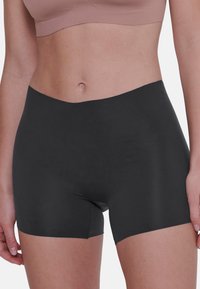 Zwarte stretchshorts met een gladde textuur, hoge tailleband en korte binnenbeenlengte. Geplaatst om de pasvorm en dekking te tonen.