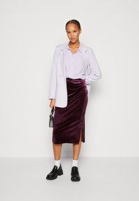 Ceriņu žakete, gaiši purpura blūze, bordo samta svārki ar sānu šķirbi, un melni platformas loafers. Apģērbs izceļas ar elegantu, modernu siluetu.