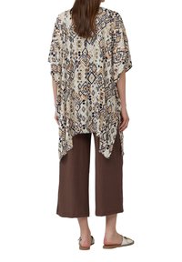 Geprinte kimono-stijl top met een geometrisch patroon in beige, bruin en zwart. Gepaarde met een bruine wijde broek en platte schoenen.
