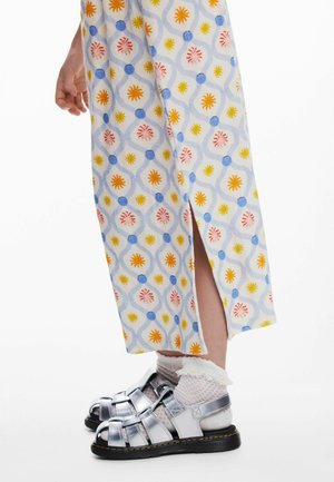 Lichtblauwe jurk met bloemmotief en zijvak, gecombineerd met glanzende zilveren sandalen en witte enkelsokken met ruches.