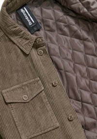 Bruin corduroy overhemdjacket met een gewatteerde binnenvoering, voorzien van een kraag, knopen en een borstzak. Maat L binnenin gemarkeerd.