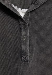 Dunkelgraues, geripptes Knopfhemd mit Kragen, versehen mit weißer Spitzenbordüre darunter und vier schwarzen Kunststoffknöpfen auf der Vorderseite.