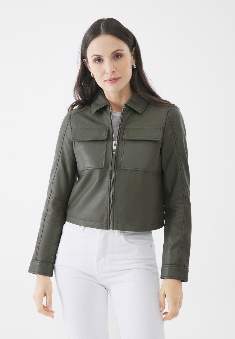 Abgeschnittene olivgrüne Lederjacke mit zwei Fronttaschen, einem Reißverschluss und einem Kragen. Tragen über einem hellfarbenen Oberteil und weißen Hosen.