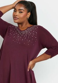 Abito bordeaux con maniche a tre quarti, caratterizzato da un'accoglienza gioiello sullo scollo e una vestibilità fluida e rilassata. Tessuto morbido.