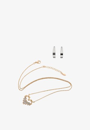 Goudkleurige ketting met een geometrische hanger, voorzien van een ontwerp met een heldere steen; gecombineerd met zilverkleurige oorringen met kleine stipaccenten.
