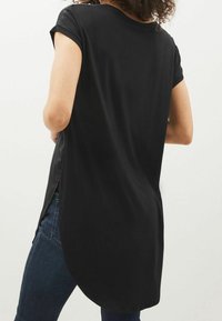 Sort kortærmet bluse med rundet kant, afslappet pasform og sidespalt. Stof ser let og glat ud, kombineret med mørke denimjeans.