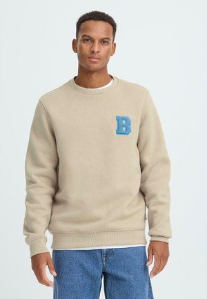Beige sweatshirt with a round neck, made of soft material; features a blue embroidered "B" logo on the chest and ribbed cuffs.