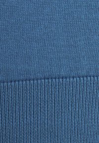 Dzianina w średnim odcieniu niebieskiego z delikatną fakturą. Spód ma prążkowany wzór, co dodaje głębi i wizualnego zainteresowania.