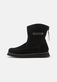 Stivale alla caviglia in suede nero con punta arrotondata, suola testurizzata e zip sul retro. Presenta un accento metallico con marchio sul lato.