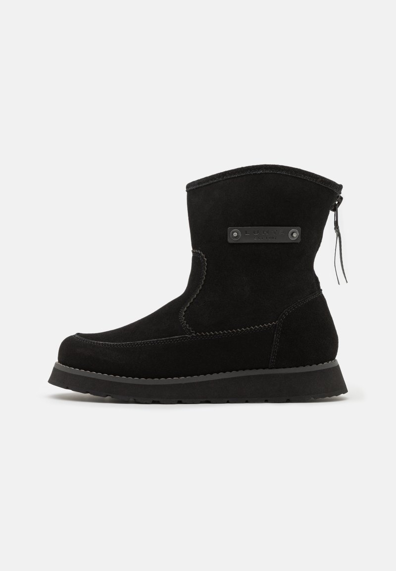 Stivale alla caviglia in suede nero con punta arrotondata, suola testurizzata e zip sul retro. Presenta un accento metallico con marchio sul lato.