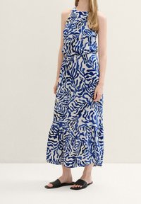 Ärmelloses Maxikleid mit einem blau-weißen abstrakten Muster, einer taillierten Taille und einem gestuften Rock, kombiniert mit schwarzen Schlappen.
