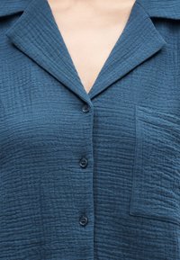 Μπλε υφασμάτινο πουκάμισο με υφή, γιακά με ανοίγματα, τρία κουμπιά στο κέντρο και τσέπη στο αριστερό μέρος.