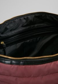 Interieur van een rode stoffen tas met een zwarte voering. Beschikt over een ritsvak en hardware met een gouden tint. Overal een soepele textuur.