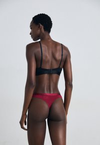 Zwart lingerieset met een minimalistisch ontwerp: een beha met verstelbare bandjes en een sluiting op de rug, gecombineerd met een rode string.