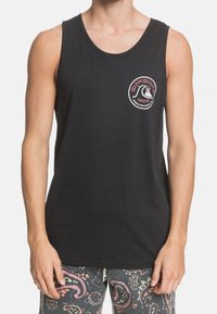 Canottiera nera in cotone con scollatura rotonda e logo Quiksilver al centro. Indossata con pantaloni corti a fantasia con motivi paisley.