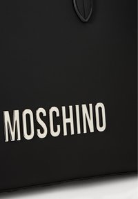 Μαύρη δερμάτινη τσάντα με μεταλλικό λογότυπο "MOSCHINO", λεία υφή με δομημένο σχήμα και διακριτική λεπτομέρεια σε στυλ φύλλου.