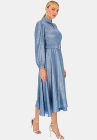 Sukienka o średniej długości, w jasnoniebieskim kolorze, wykonana z błyszczącego materiału, z wysokim kołnierzem, bufkami oraz paskiem w talii z złotą klamrą.