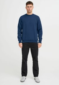 Sudadera azul marino con cuello redondo, puños y dobladillo acanalados, combinada con pantalones negros y zapatillas grises. Textura suave, diseño minimalista.