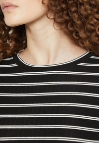 Svartvit randig topp med rund halsringning, tillverkad av ribbat tyg, med alternerande tunna och tjocka ränder.