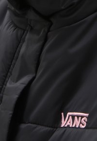 Nærbillede af en sort polstret jakke med pink broderet Vans-logo på stofoverfladen.