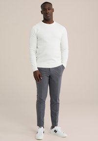 Witte gebreide trui, grijze op maat gemaakte broek, en witte sneakers met zwarte accenten. De outfit heeft een getailleerd silhouet met geribde manchetten.
