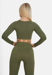 Olivenfarbenes Activewear-Set bestehend aus einem gekürzten Langarmtop und hochgeschnittenen Leggings, beide mit strukturierter Oberfläche und figurbetontem Design.