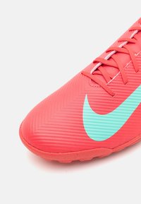 Punainen urheilujalkine, jossa on kuvioitu pinta, sisältää vaaleansinisen Nike-swooshin ja vaaleanpunaiset nauhat. Muodikas kärki ja kumipohja näkyvissä.