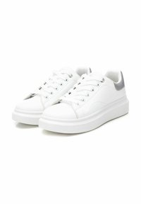Zapatillas deportivas sintéticas blancas con punta redondeada, suela plana y acentos plateados en el talón. Presentan seis ojales para cordones y textura suave.