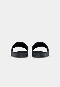 Ein Paar schwarze Rutschsandalen mit dicken Riemen, von vorne auf einem weißen Hintergrund gezeigt.