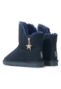 Botas de tobillo de ante azul marino con forro de pelaje sintético, que cuentan con un cierre lateral y un detalle de charm de estrella dorada. Suelas planas de goma con agarre texturizado.