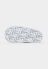 Semelle d'une chaussure blanche avec un motif triangulaire texturé et un logo de marque rectangulaire au centre sur un fond clair uni.