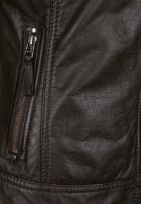 Nahaufnahme einer braunen Lederjacke mit einer Reißverschlusstasche, strukturiertem Material und sichtbaren Nähten entlang der Ränder.