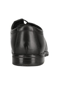 Chaussure habillée en cuir noir vue de l'arrière, montrant des détails cousus et un petit talon empilé sur fond blanc.