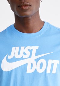 T-shirt de algodão azul claro com o ousado texto branco "JUST DO IT" e o logo do swoosh da Nike; design clássico de gola redonda, textura suave.