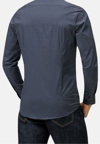 Uomo che indossa una camicia attillata a maniche lunghe blu navy con piccoli pois bianchi, abbinata a jeans blu scuro, mostrato di spalle.
