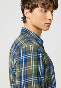 Camicia in flanella con bottoni, caratterizzata da un motivo a quadri nei toni del blu, verde e oliva, con colletto classico e tessuto di peso medio.