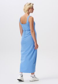 Robe maxi en coton bleu avec encolure dégagée, taille ajustée et jupe ample. Portée avec des baskets blanches et des chaussettes mi-mollet.