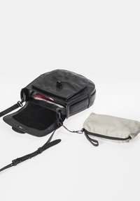 Schwarze Lederhandtasche mit glatter Oberfläche, runder Form, Vorderklappenverschluss, Innenfächern und einem abnehmbaren gestreiften Beutel.