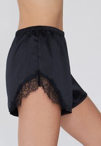 Zwarte satijnen shorts met een elastische tailleband, voorzien van kant aan de zoom voor een contrast in textuur en een gedetailleerd bloemenpatroon.
