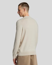 Beige kötött pulóver, kerek nyakkal, hosszú ujjakkal és sima felülettel. Bordás mandzsettákkal és aljjal rendelkezik, hátulról látható.