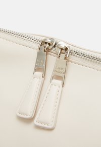 Beige leather zippered pouch featuring dual silver zippers with stitched accents; smooth texture and minimalist design.