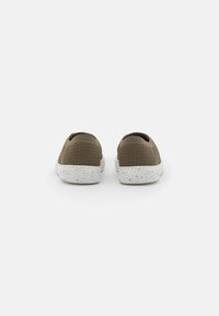 Chaussures slip-on en mailles marron avec un dessus texturé et des semelles en caoutchouc blanches à pois, présentant un profil bas et un design minimaliste.