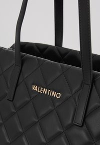 Svart quiltad läderhandväska med dubbla handtag och en gyllene "VALENTINO"-logotyp på framsidan. Har en strukturerad design och en slät yta.