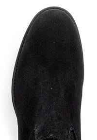 Zwarte suède enkelboot met een ronde neus en minimale stiksels langs de randen. Zachte textuur, eenvoudig ontwerp, licht verhoogde hak.