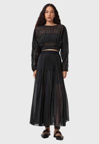 Top cropped trasparente nero con maniche lunghe e gonna maxi nera plissettata. Tessuto liscio con vita arricciata e design a strati. Calzature nere.
