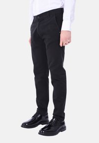 Pantaloni di cotone neri con vestibilità dritta e zip. Presentano tasche frontali e una marcatura discreta. Abbinati a scarpe nere lucide.