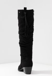 Botte noire haute jusqu'au genou en daim avec un design ample. Comprend un accent à pampilles et un talon bas et solide pour la stabilité. Fermeture éclair latérale.