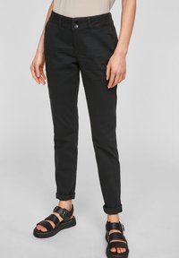 Černé bavlněné kalhoty slim fit s knoflíkovým zapínáním, ohrnutými nohavicemi a bočními kapsami, doplněné černými sandály na pásky.