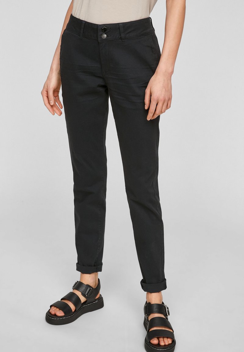Černé bavlněné kalhoty slim fit s knoflíkovým zapínáním, ohrnutými nohavicemi a bočními kapsami, doplněné černými sandály na pásky.
