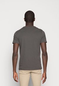 Šedé bavlněné tričko s krátkými rukávy, kulatým výstřihem a mírně strukturovaným povrchem. Pohled zezadu ukazuje jednoduché, čistě střižené zakončení.